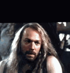 a man with long hair and a beard is looking at the camera in a dark room .