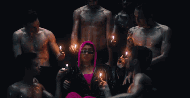 a woman in a pink hood is surrounded by men holding lit candles