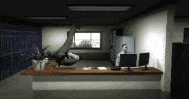 a man is sitting at a desk with two monitors and a plant