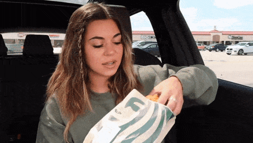 a woman is sitting in a car holding a bag that says gf on it