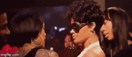 a group of women are standing next to each other in a room . one of the women is wearing sunglasses and earrings .