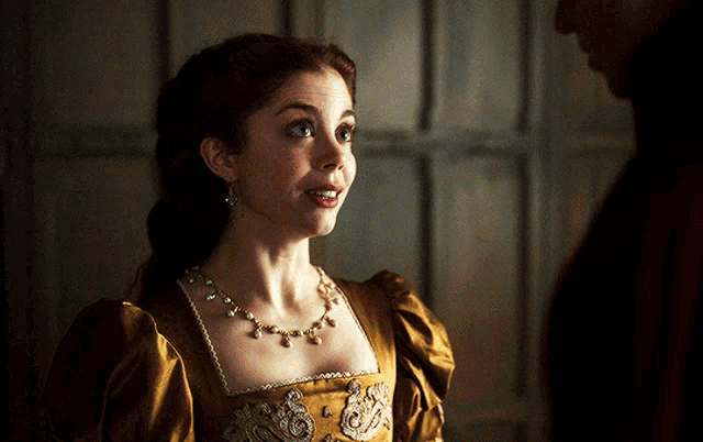a woman in a gold dress and necklace looks surprised