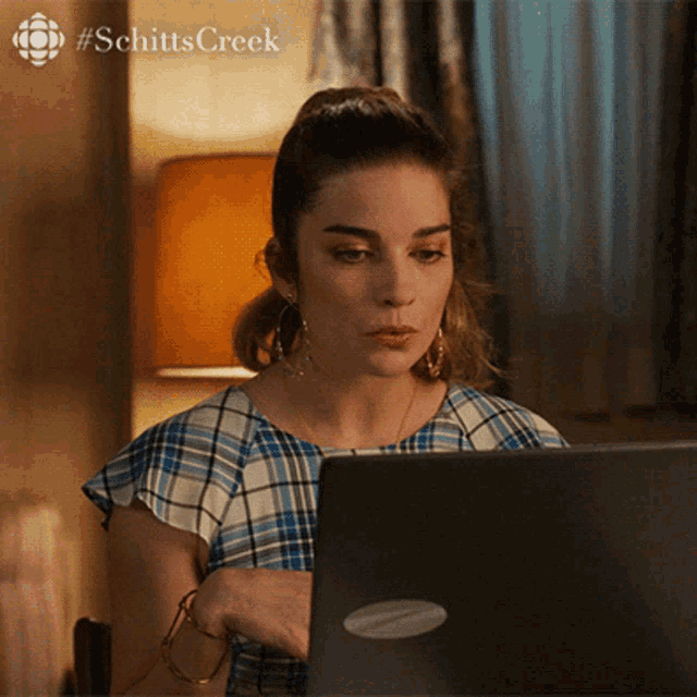 a woman sitting in front of a laptop with the word schitts creek on the bottom right