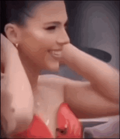 a woman in a red dress is smiling and holding her hand to her ear .