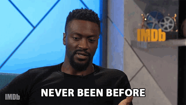 a man with a beard is sitting in front of a sign that says never been before
