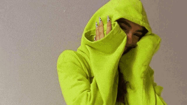 a woman is wearing a neon green hoodie and covering her face with her hands .