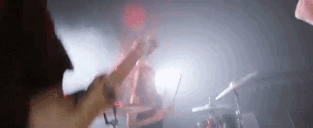 a man is playing a guitar in front of a drum set in a dark room .