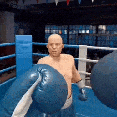 a bald man is wearing blue boxing gloves in a boxing ring .