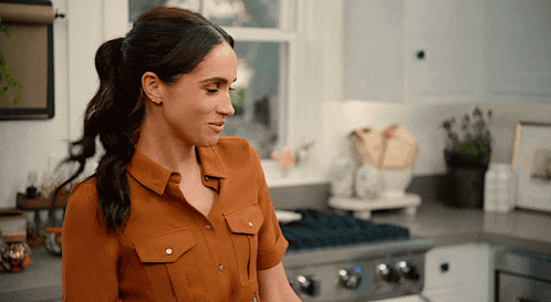a woman standing in a kitchen wearing a brown shirt