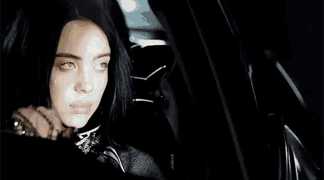 a woman is sitting in the driver 's seat of a car at night .