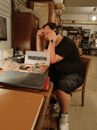 a man wearing headphones sits at a desk with a sign on it that says peaceeaatelb