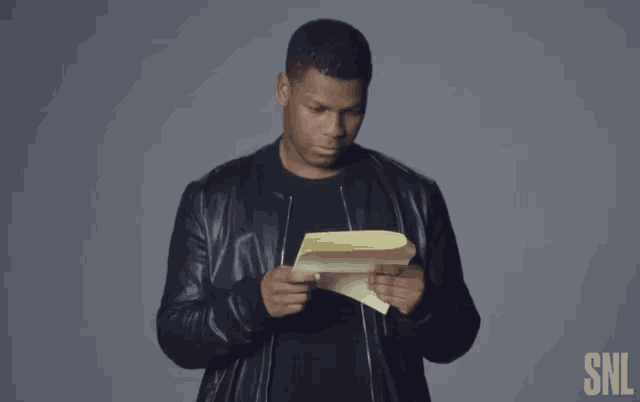 a man in a black jacket is holding a piece of paper and smiling .