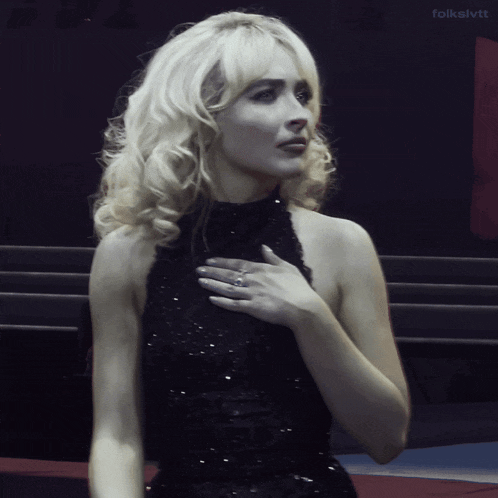 a blonde woman in a black dress with folkslvtt written on the bottom right