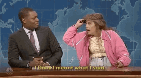 a man in a suit and tie is sitting at a desk with a woman in a pink jacket .