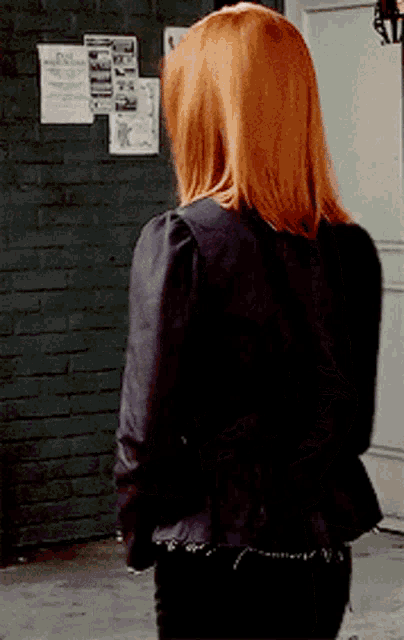 a woman with red hair is standing in front of a brick wall with papers on it