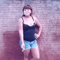 a woman in a black tank top and blue shorts is smoking a cigarette
