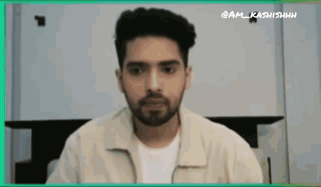 a man with a beard is wearing a tan jacket and white shirt