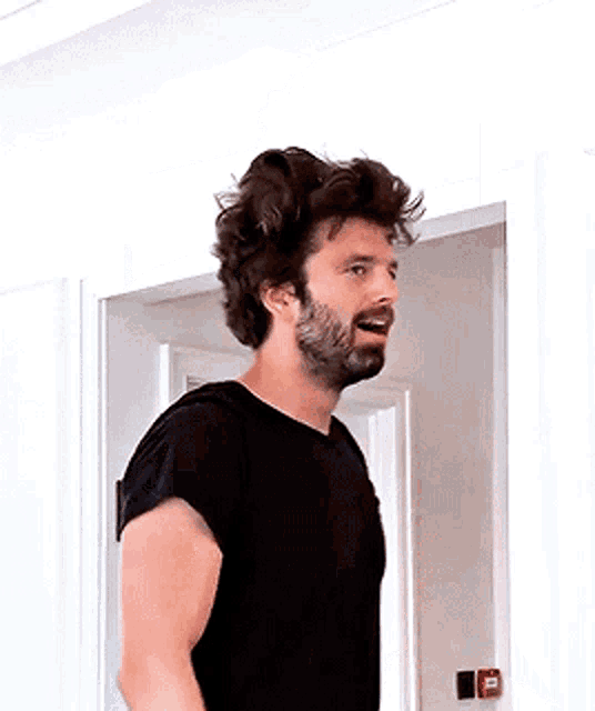 a man with a beard and a black shirt is standing in a doorway .