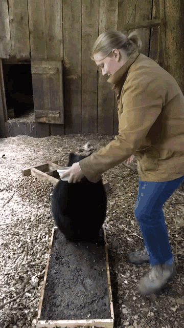 a woman in a brown jacket is playing with a black rabbit