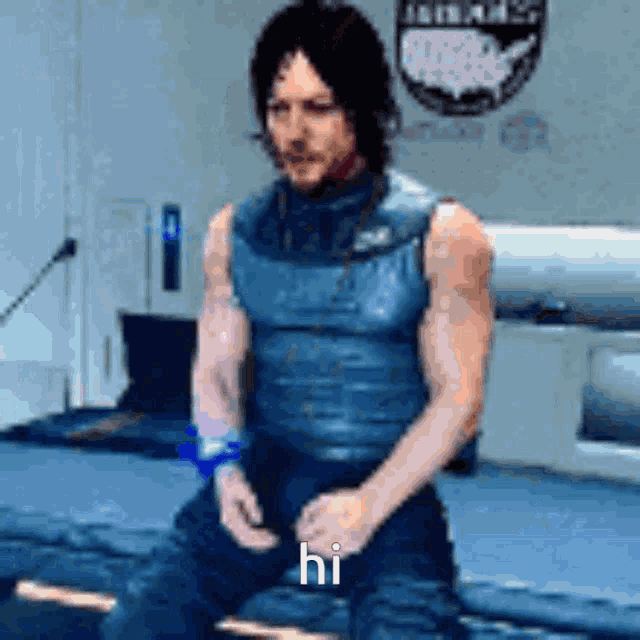 a man in a blue vest is sitting on a bed and says hi
