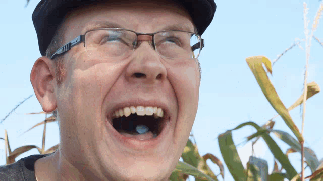 a man wearing glasses and a hat is laughing with his mouth wide open