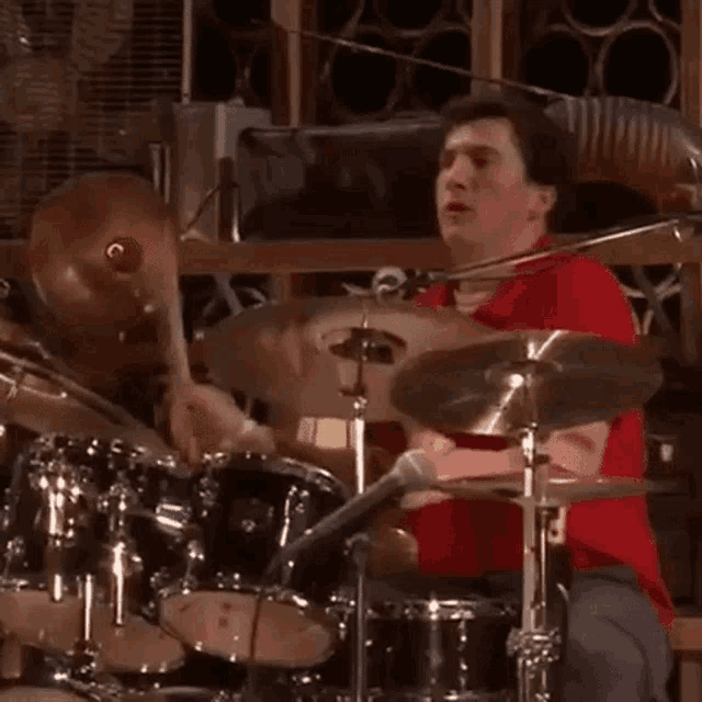 a man in a red shirt is playing drums in a dark room .