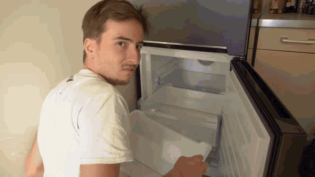 a man in a white shirt is opening a fridge door