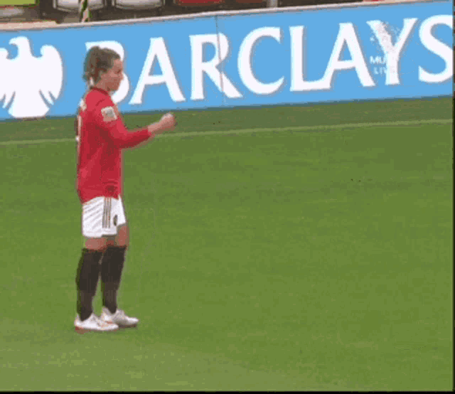 two soccer players shaking hands on a field with a barclays banner behind them