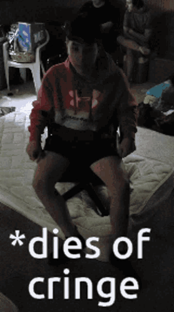 a boy in a red under armour sweatshirt sits on a mattress