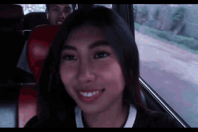 a woman is smiling while sitting in a bus with a man behind her