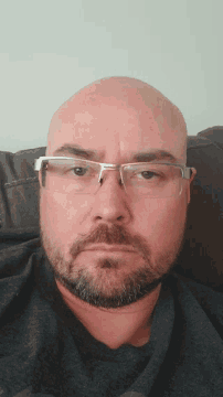 a bald man with glasses and a beard is laying down