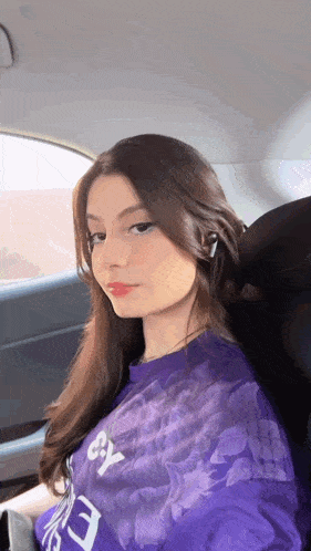 a girl in a purple shirt is sitting in the back seat of a car