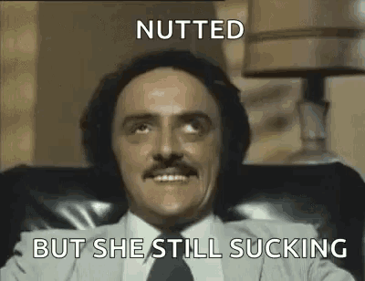 a man in a suit and tie is sitting in a chair with the words `` nutted but she still sucking '' .