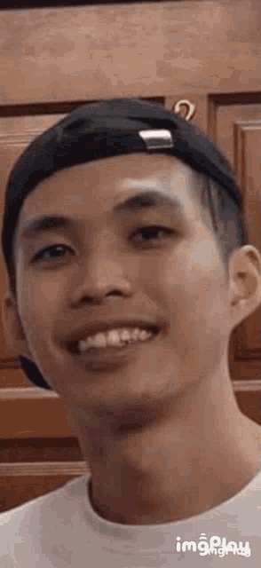 a young man wearing a baseball cap and a white shirt is smiling .