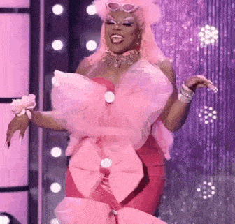 a drag queen is wearing a pink dress with a large pink bow on the front .