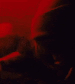 a close up of a person 's face in a dark room with a red background .