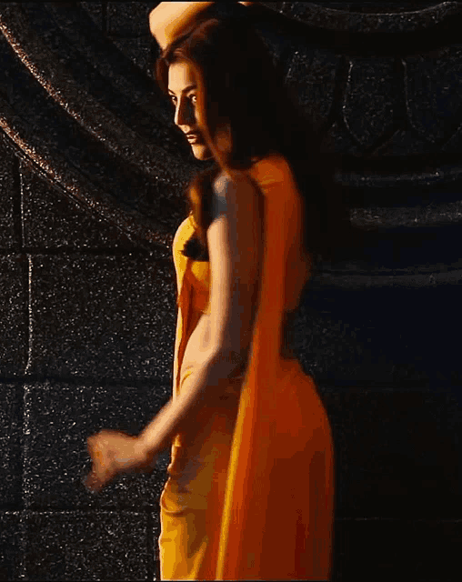 a woman in a yellow dress is dancing in front of a wall .