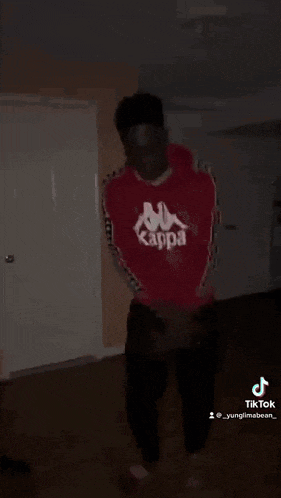 a man in a red kappa sweatshirt is dancing in a dark room .