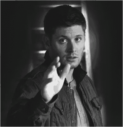 a black and white photo of a man in a jacket pointing at the camera .
