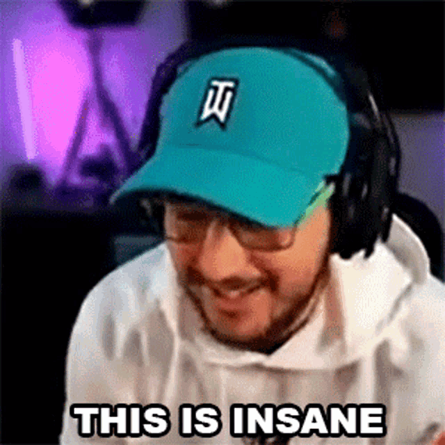 a man wearing a hat and headphones is smiling and saying `` this is insane '' while playing a video game .