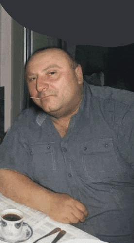 a man is sitting at a table with a cup of coffee in front of him .