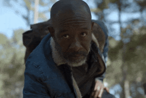 a man with a beard wearing a denim jacket looks at the camera