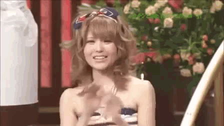 a woman without a shirt is smiling and clapping her hands in front of a flower arrangement .