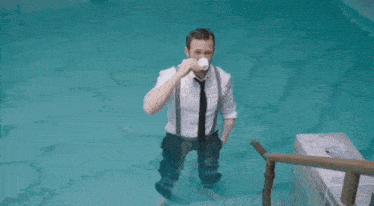 a man in a suit and tie is sitting on a bench in a bathroom holding his shoes .