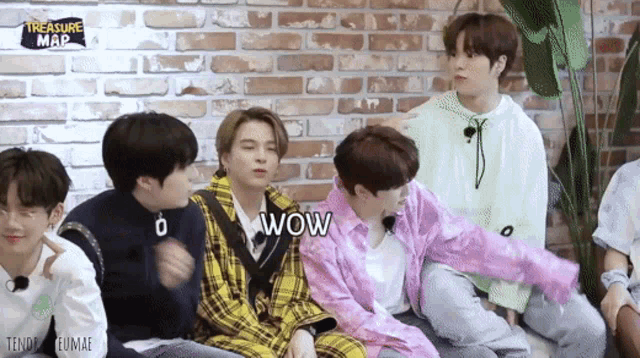 a group of young men are sitting next to each other in front of a brick wall and one of them is saying wow .