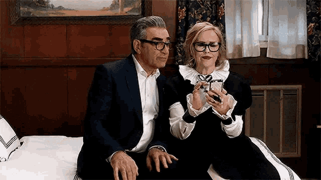 a man and a woman are sitting on a bed looking at their cell phones .