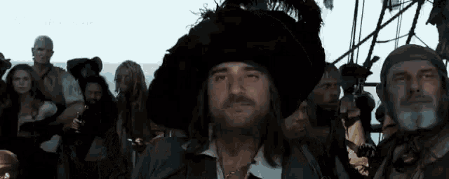 a man with long hair and a beard wearing a pirate hat is standing in front of a crowd of people .