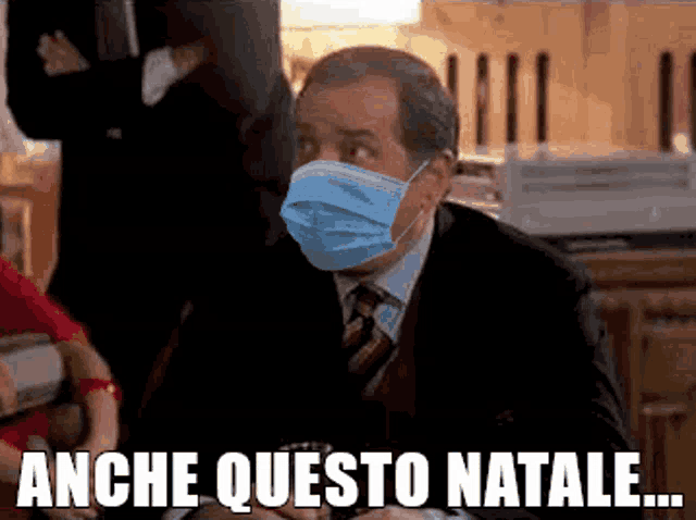 a man in a suit and tie wearing a face mask with the words anche questo natale below him
