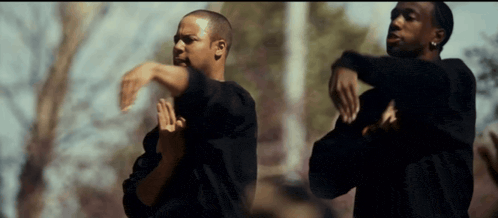 two men in black shirts are dancing together in a park