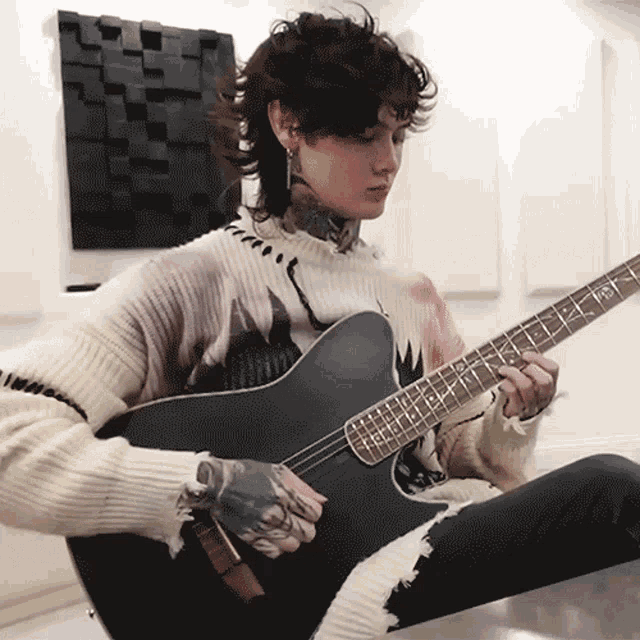 a man in a sweater is playing a guitar with the letter e on it